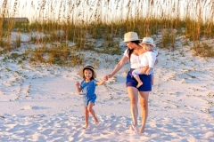 Mother holding her baby while walking on the sand, holding hands with her young daughter during a family beach session