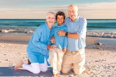Grandparents kneeling in the sand, embracing their grandson during a beach family session