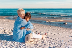 Close-up of a grandmother hugging her grandson, both smiling warmly during a beach photoshoot