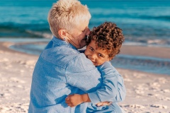 Grandmother hugging her grandson while sitting on the beach, with waves in the background