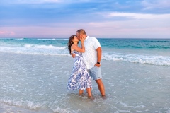 Couple embracing on the shoreline at sunset, with waves crashing softly and a serene twilight sky in the background