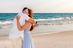 Newly engaged couple embracing on a sandy beach, with the ocean waves and soft evening light in the background